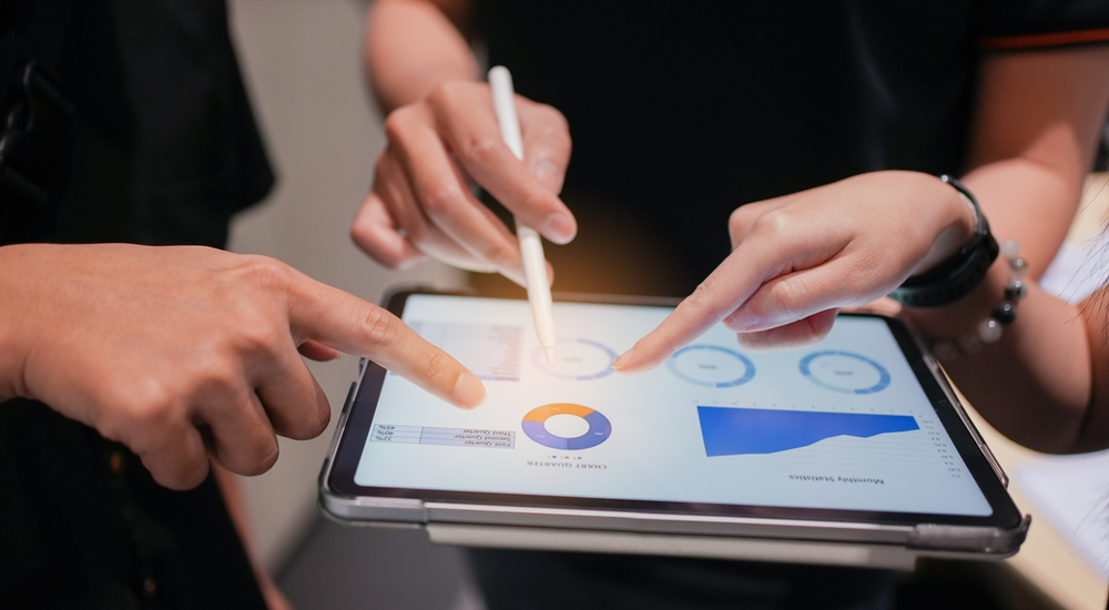 Three individuals looking at graphs on a tablet. 